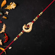 Golden Peacock Feather Rakhi With Red Thread And Kundan Detailing thumbnail 1